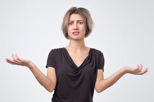 Woman is looking perplexed and shrugging her shoulders while holding her hands up.