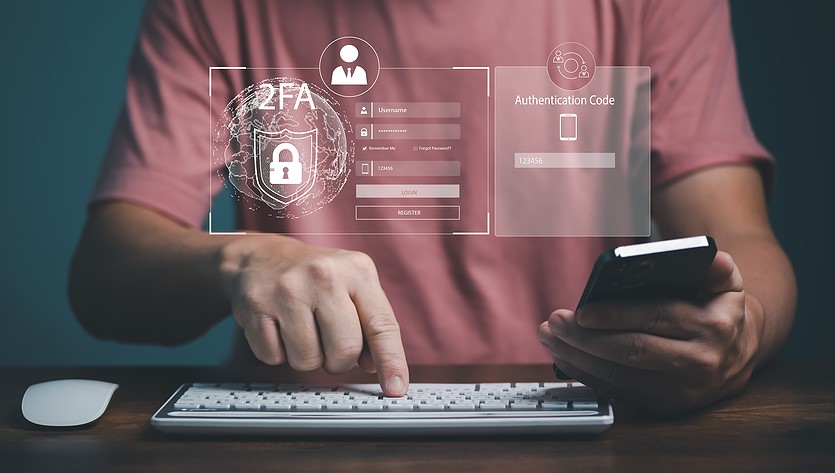 A person is holding a mobile phone while pressing a key on a keyboard. Virtual images of financial symbols float in the foreground.