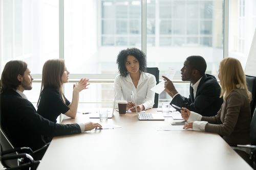 Business professionals are seated around a board room table during a meeting.
