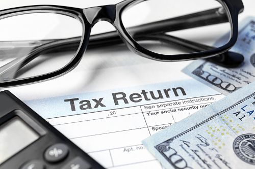 Tax return form, glasses, calculator and dollars on table