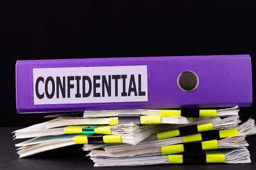 A purple binder labeled "CONFIDENTIAL" rests on top of several stacks of paper documents clipped together with yellow and black binder clips, all set against a black background.
