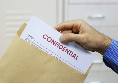 Cropped view image of a man handling confidential documents placing them inside a brown manilla envelope for mailing